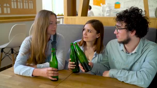 Трое друзей сидят в кафе, пьют воду или пиво и весело общаются — стоковое видео