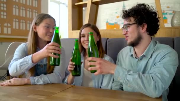 Трое друзей сидят в кафе, пьют воду или пиво и весело общаются — стоковое видео
