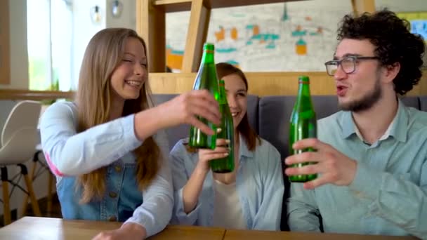 Tres amigos se sientan en un café, beben agua o cerveza y se divierten comunicándose. Movimiento lento — Vídeos de Stock