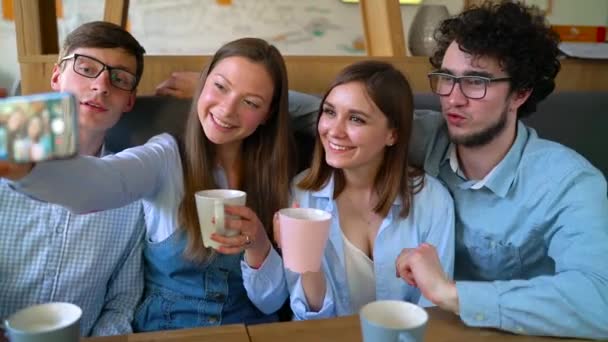 Amigos sorridentes sentam-se em um café, se divertem se comunicando e fazem selfie — Vídeo de Stock