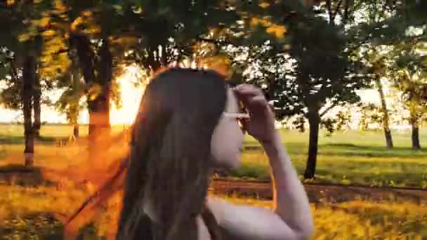 Γυναίκα με τα γυαλιά χρησιμοποιεί ένα smartphone ενώ το περπάτημα στο δρόμο, στο ηλιοβασίλεμα — Αρχείο Βίντεο