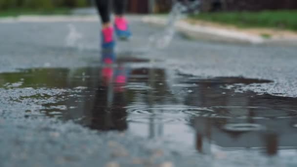 在运动鞋中关闭跑步者腿部的慢动作镜头。女子运动男子在公园户外慢跑, 步入泥泞的水坑. — 图库视频影像