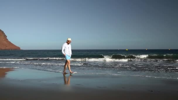 Gelukkig man wandelen langs het strand van de Oceaan bij zonsondergang. Concept van zorgeloos moderne leven. Tenerife, Canarische eilanden — Stockvideo