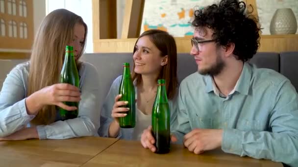 Três amigos se sentam em um café, bebem água ou cerveja e se divertem se comunicando — Vídeo de Stock