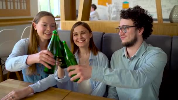 Tre amici si siedono in un caffè, bevono acqua o birra e si divertono a comunicare — Video Stock