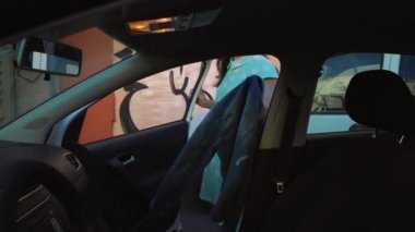 Kadın araba koltuğunda bir ceket koymak ve motoru çalıştırmayı planlayan şoför koltuğunda oturur