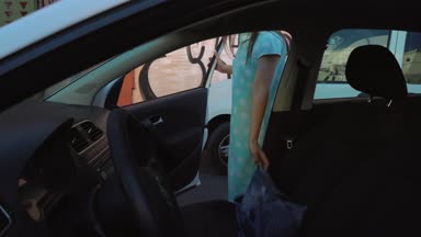 Kadın araba koltuğunda bir ceket koymak ve motoru çalıştırmayı planlayan şoför koltuğunda oturur