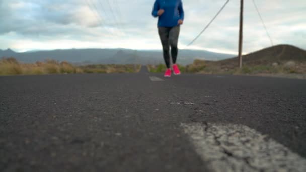 Беговая обувь - женщина, завязывающая шнурки на пустынной дороге в горной местности. Медленное движение — стоковое видео