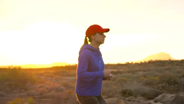 Женщина бежит по пустынной местности на закате. Горы на заднем плане. Медленное движение — стоковое видео