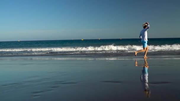 O homem feliz corre ao longo da praia oceânica ao pôr-do-sol. Conceito de vida moderna despreocupada. Tenerife, Ilhas Canárias. Movimento lento — Vídeo de Stock