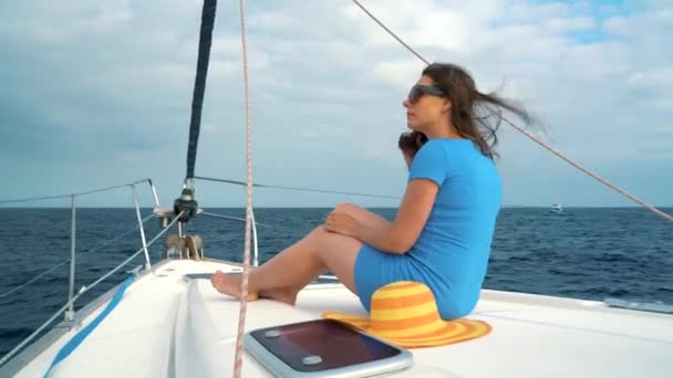 Mujer con un sombrero amarillo y vestido azul agitando el pelo y sonriendo en el yate en la temporada de verano en el océano — Vídeo de stock