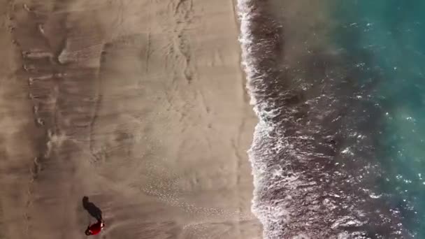 Vista superior de uma mulher em vestido vermelho andando descalça ao longo da praia do oceano de areia molhada — Vídeo de Stock