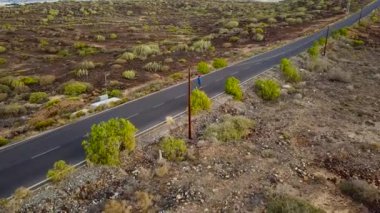 Kadının havadan görünümü görünümü Günbatımında geri ıssız asfalt yol boyunca çalışır. Arka planda dağlar