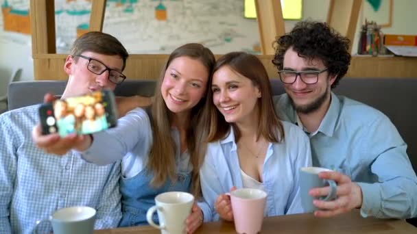 Amigos sonrientes se sientan en un café, se divierten comunicándose y hacen selfie — Vídeos de Stock