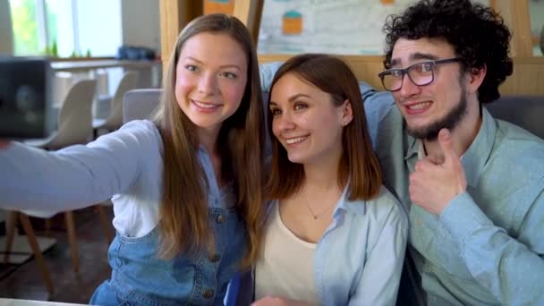 Tres amigos se sientan en un café, se divierten comunicándose y hacen selfies. Movimiento lento — Vídeos de Stock