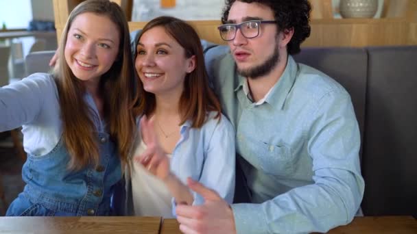 Três amigos se sentam em um café, se divertem se comunicando e fazem selfie. Movimento lento — Vídeo de Stock