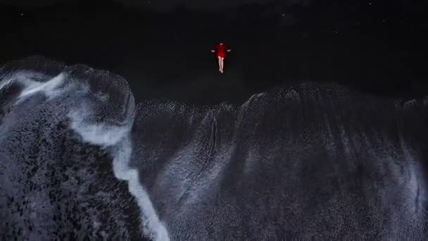 Luchtfoto van een meisje in een rode jurk zittend op het strand met zwart zand. Tenerife, Canarische eilanden, Spanje — Stockvideo