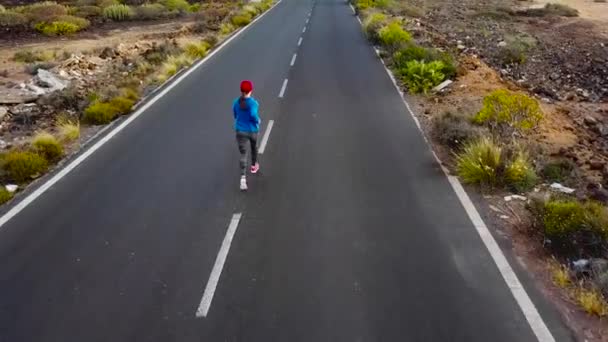 若い女性の空撮はビュー人けのないアスファルトの道路に沿って夕暮れ 戻って実行されます 背景の山 — ストック動画