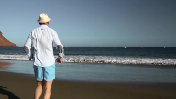 Gelukkig man loopt naar de oceaan strand bij zonsondergang. Concept van zorgeloos moderne leven. Tenerife, Canarische eilanden — Stockvideo