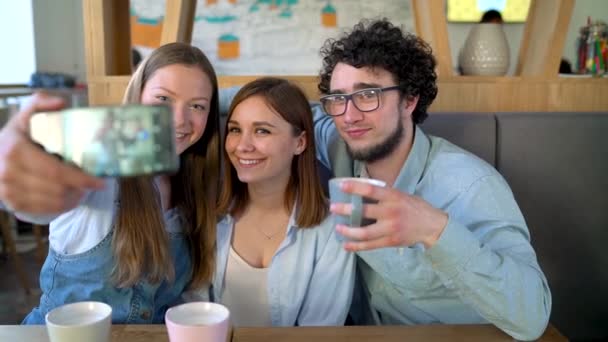 Três amigos se sentam em um café, se divertem se comunicando e fazem selfie — Vídeo de Stock