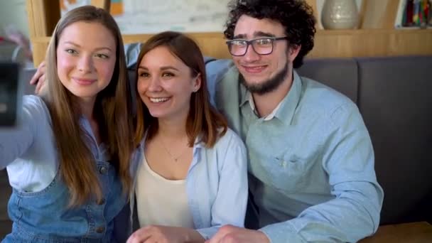 Три друга сидят в кафе, весело общаются и делают селфи — стоковое видео