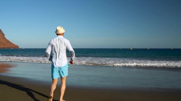 O homem feliz corre para a praia do oceano ao pôr-do-sol. Conceito de vida moderna despreocupada. Tenerife, Ilhas Canárias. Movimento lento — Vídeo de Stock