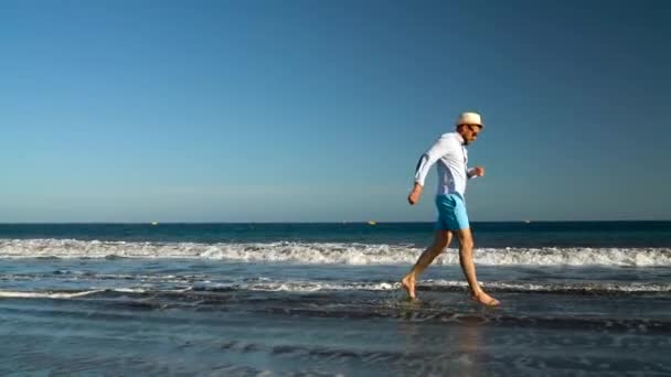 El hombre feliz corre a lo largo de la playa al atardecer. Concepto de vida moderna despreocupada. Tenerife, Islas Canarias. Movimiento lento — Vídeo de stock