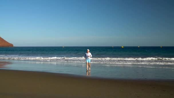 Gelukkig man loopt vanaf de oceaan strand bij zonsondergang. Concept van zorgeloos moderne leven. Tenerife, Canarische eilanden — Stockvideo