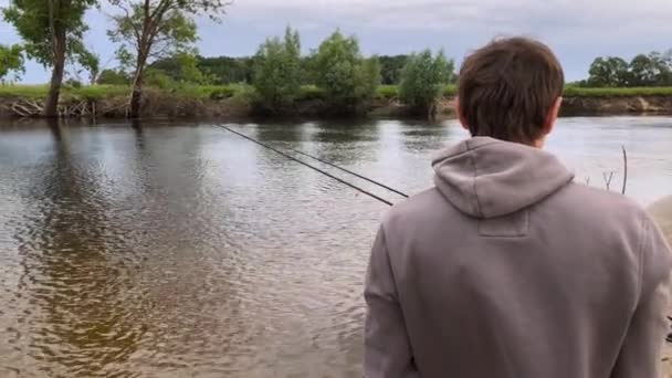 Pescador com uma vara de pesca na margem do rio. Homem pescador pega um peixe. Conceito de uma fuga rural — Vídeo de Stock