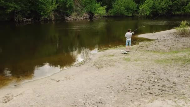 Fiskare med ett fiskespö på Älvstranden. Mannen fiskare fångar en fisk. Begreppet en lantlig semester — Stockvideo