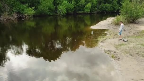 Vista aérea del pescador con caña de pescar en la orilla del río. El pescador atrapa un pez. Concepto de escapada rural — Vídeos de Stock