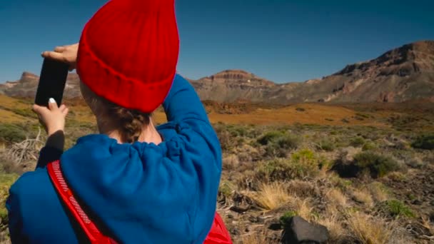 活跃的徒步旅行妇女徒步旅行在 Teide 国家公园并且在智能手机上做相片风景。慢动作。在特内里费岛, 加那利群岛, 西班牙有背包的高加索年轻女子 — 图库视频影像