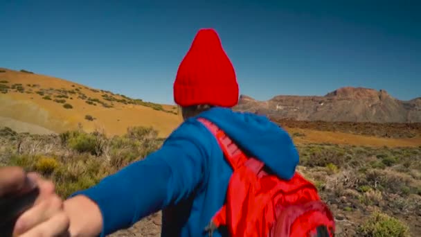 Peşimden - kırmızı şapkalı adamlar el çekerek sırt çantası ile mutlu bir genç kadın. El ele yürüyüş atmak Teide Milli Parkı, Tenerife, Kanarya Adaları, İspanya. — Stok video