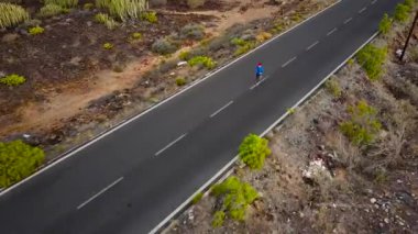 Kadının havadan görünümü, gün batımında ıssız asfalt yol boyunca çalışır. Arka planda dağlar