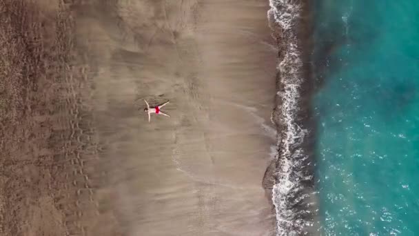 赤いパンツの男性の空撮は、黒砂のビーチにあります。テネリフェ島のカナリア諸島、スペイン — ストック動画