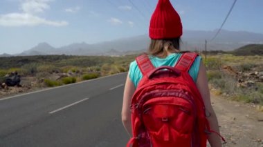 Güneşli bir yolda otostop ve yürüyüş gezgin kadın. Bir güneşli ülke yolda bir yolculuğa başlamak için bir gezintiye arayan backpacker kadın. Ağır çekim
