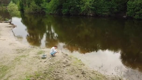 Pescador com uma vara de pesca na margem do rio. Homem pescador pega um peixe. Conceito de uma fuga rural — Vídeo de Stock