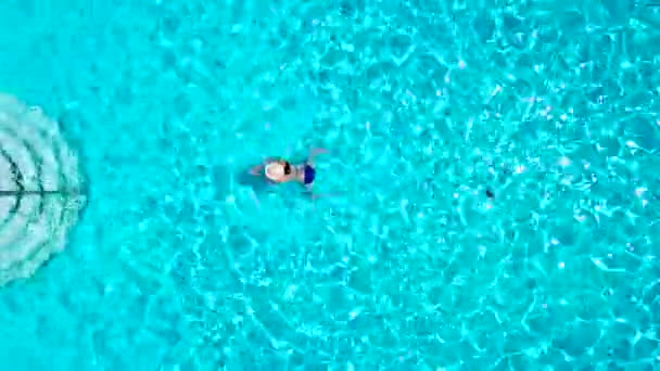 Uitzicht vanaf de top als een vrouw in een blauwe zwembroek in het zwembad zwemt — Stockvideo