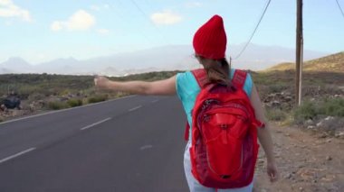 Güneşli bir yolda otostop ve yürüyüş gezgin kadın. Bir gezintiye arayan backpacker kadın yağdırdığı ülke yolda bir yolculuğa başlamak için