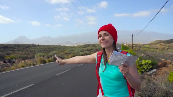 Viaggiatore donna autostop su una strada soleggiata e passeggiate. Donna zaino in spalla in cerca di un passaggio per iniziare un viaggio su una strada di campagna illuminata dal sole. Rallentatore — Video Stock