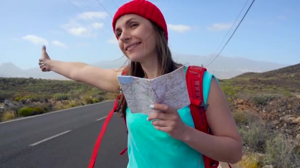 日当たりの良い道路でヒッチハイクと徒歩旅行者の女性。バックパッカー女は、太陽に照らされた国の道路の旅を開始する乗車時間を探しています。スローモーション — ストック動画