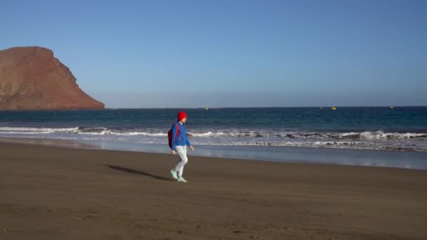 Aktive Wanderin spaziert am Strand. Kaukasische junge Frau mit Rucksack auf Teneriffa, Kanarischen Inseln, Spanien — Stockvideo