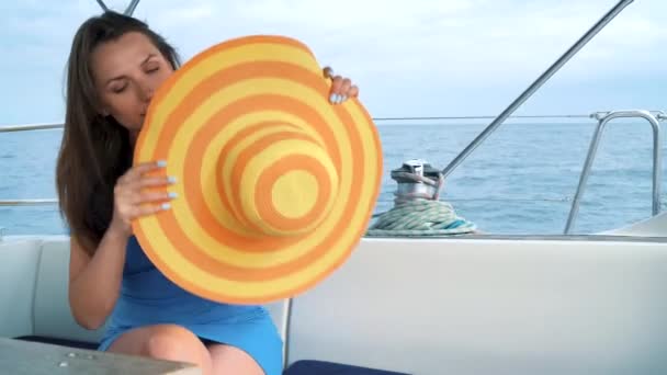 Женщина в жёлтой шляпе и синем платье отдыхает на борту яхты в летний сезон у океана — стоковое видео