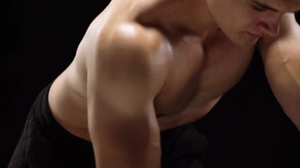 Man flexes his hands with dumbbells, training his back on a black background in the studio — Stock Video