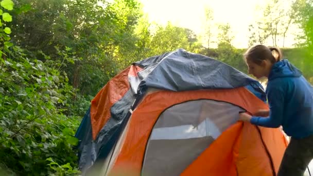 Mulher está colocando uma tenda turística na margem do rio e descansa nele — Vídeo de Stock