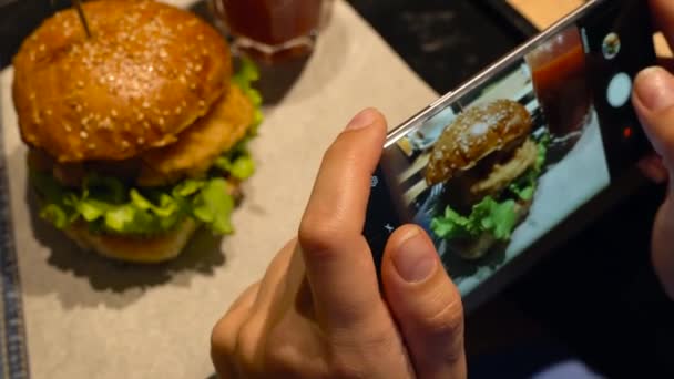 Girl makes a photo of burger and tomato juice on a smartphone in a cafe close up — Stock Video