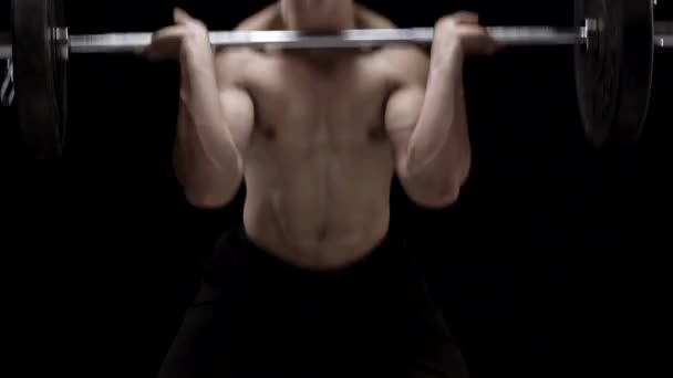 Man is doing exercises with a barbell, training on a black background in the studio — Stock Video