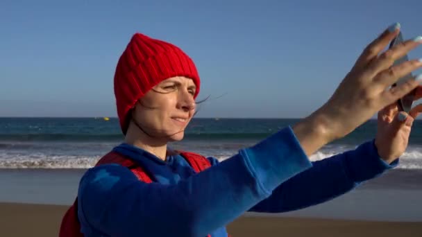Die aktive Wanderin geht am Strand spazieren und macht Selbstfotos mit ihrem Smartphone. Kaukasische junge Frau mit Rucksack auf Teneriffa, Kanarischen Inseln, Spanien — Stockvideo