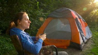 Kadın bir koltuk nehir kıyısında bir çadırın yakınında çay içiyor