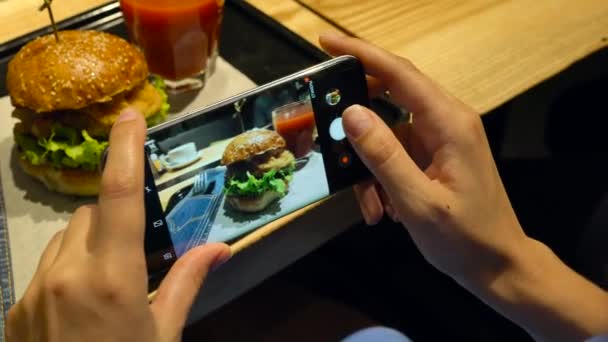 Menina faz uma foto de hambúrguer e suco de tomate em um smartphone em um café de perto — Vídeo de Stock